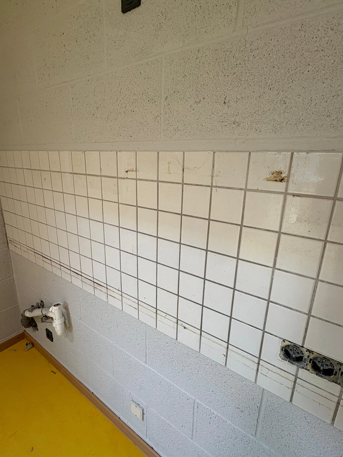 Fliesenwand mit Mörtelschleier und verschmutzten Fugen