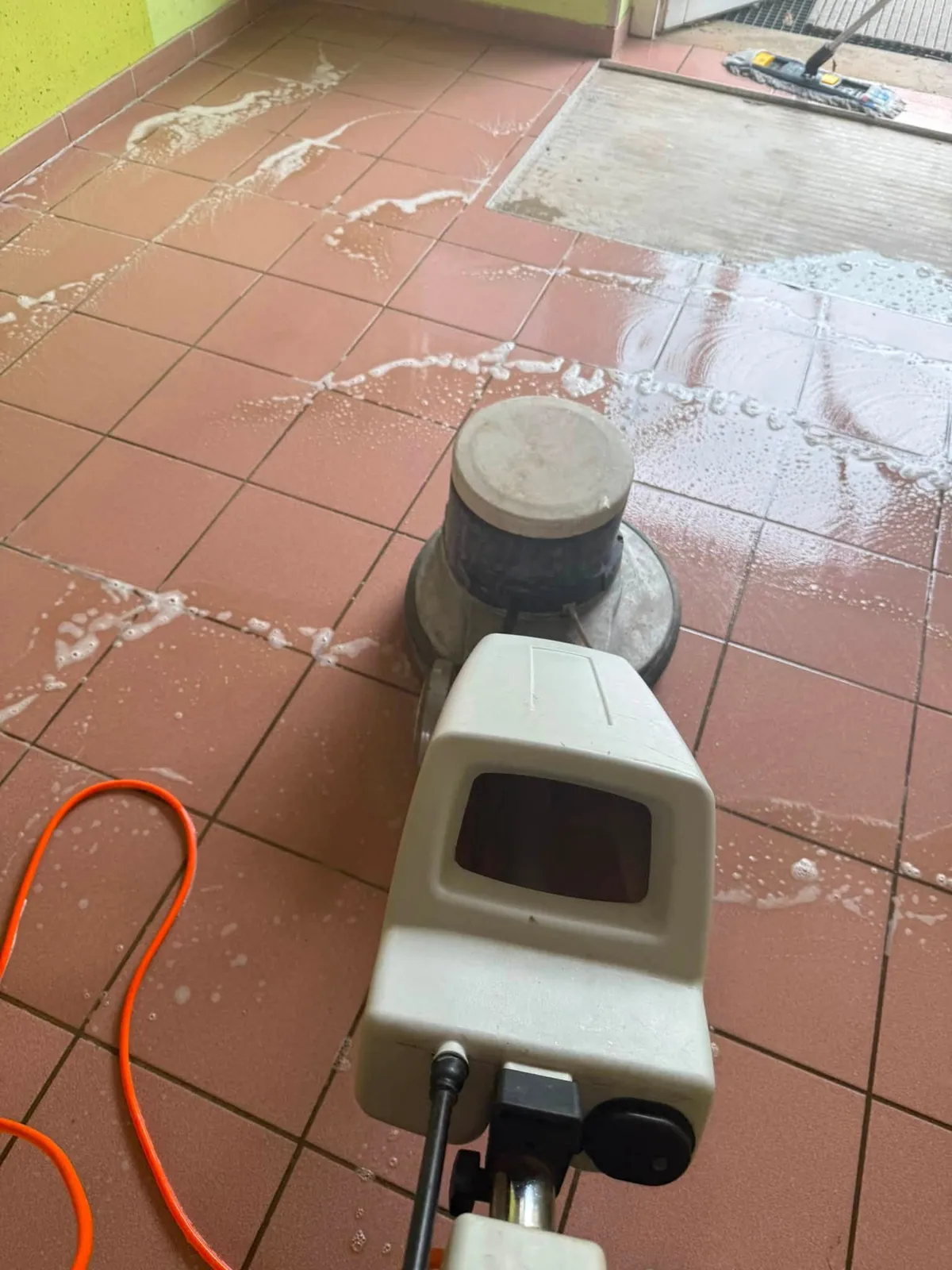 Einscheibenmaschine auf rotem Fliesenboden, Reinigungslösung auf der Fläche