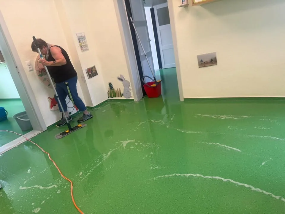 Mitarbeiterin reinigt den Randbereich eines Bodenbelags von Hand