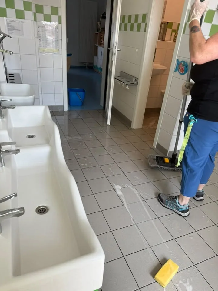 Mitarbeiterin reinigt den Boden eines Sanitärraums von Hand