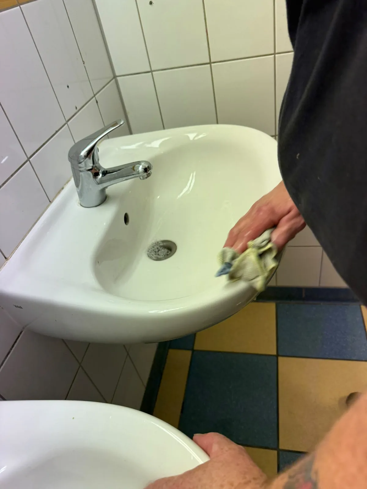 Hand mit Reinigungstuch wischt ein Waschbecken samt Armatur aus