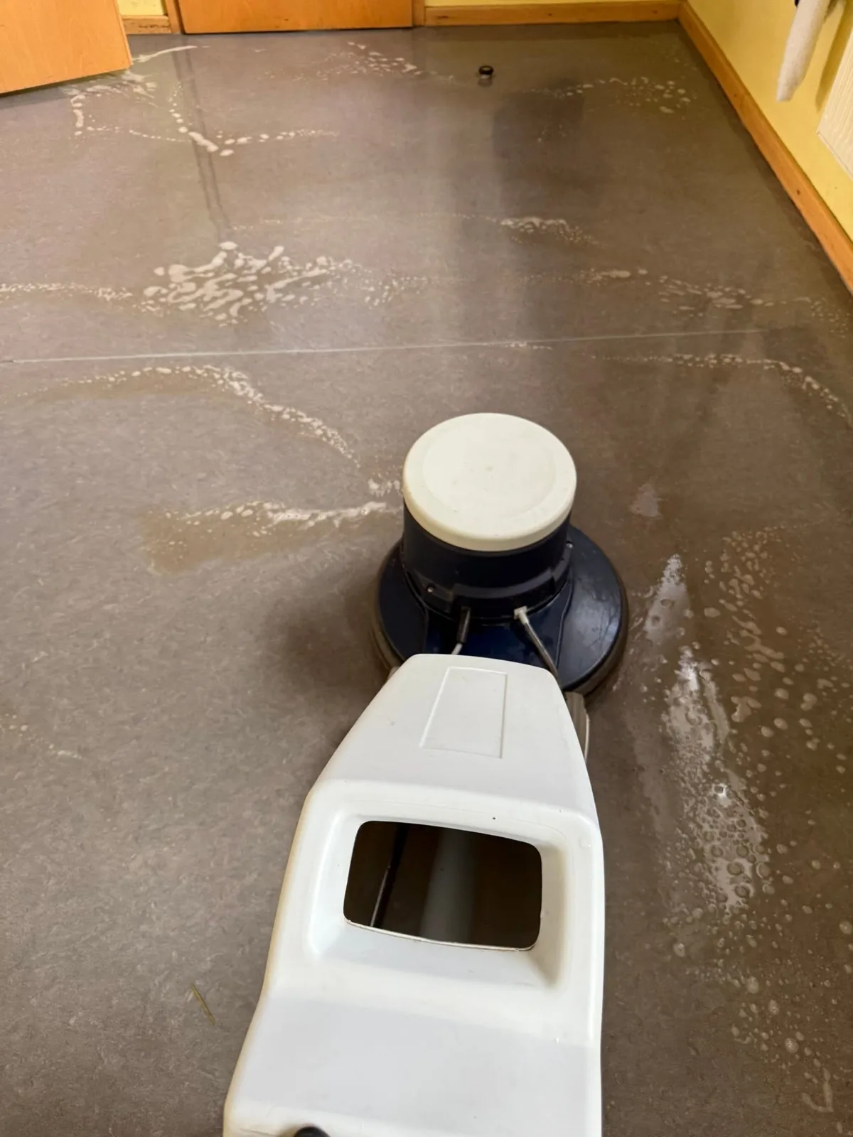 Gelöster Pflegefilm als trübe Flotte auf dem Bodenbelag neben der Maschine